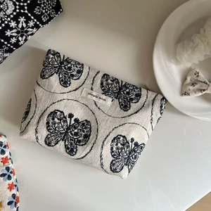 Detail of a beige linen makeup pouch featuring elegant black butterfly embroidery