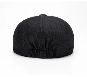 Detail view of the elastic band at the back of a black denim newsboy cap