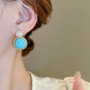 Close-up of vintage earrings with a faux pearl and turquoise stone on a gold-plated base