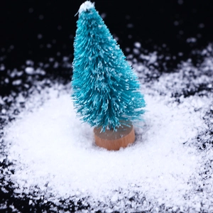 Detailed view of artificial snow powder on a mini flocked Christmas tree with wooden base