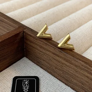 Macro detail of gold V-shaped chain tassel earrings on a dark wooden jewelry box