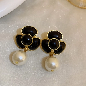 Detailed close-up of vintage gold-rimmed black clover earrings with dangling white pearls