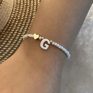Detail of white beaded bracelet with gold heart and letter G pendant on woman's wrist