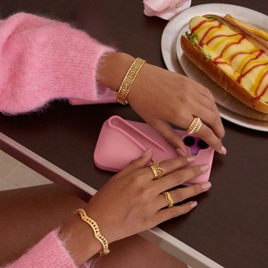 Vue détaillée d'un bracelet doré géométrique ajouré et de bagues portés par un mannequin