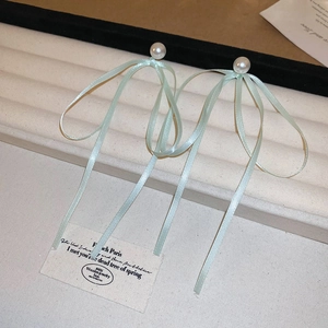 Detail view of light green satin ribbon bow earrings with elegant white pearls on a display