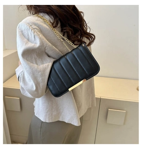 Detail of a black quilted crossbody bag featuring elegant gold chain strap and metal trim