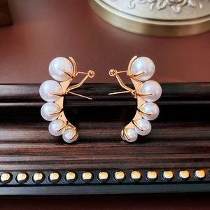 Detailed view of elegant gold curved earrings with five white pearls on a wood surface