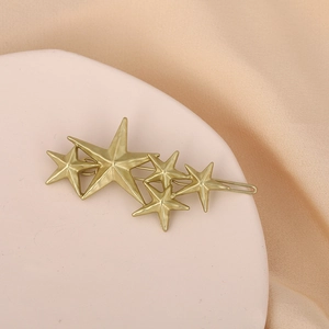 Golden multi-star hair clip featuring textured pentagrams on a beige satin background