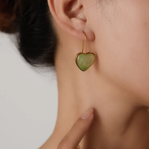 Close-up of gold heart earrings with green jade texture worn by a model in soft light