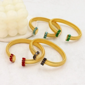 Bracciale rigido a C dorato con zirconi colorati su superficie di marmo chiaro