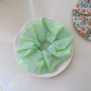 Close-up of mint green pleated fabric scrunchie with subtle floral pattern and soft texture