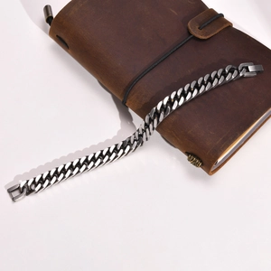 Polished stainless steel Cuban link chain bracelet on a brown leather notebook