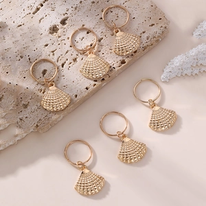 Detailed view of six golden conch shell pendant earrings on a textured stone base