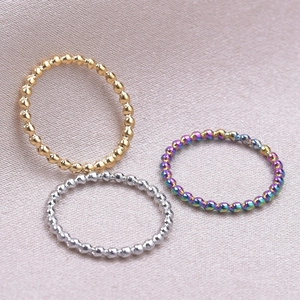 Detailed view of gold, silver and rainbow beaded rings on textured fabric background