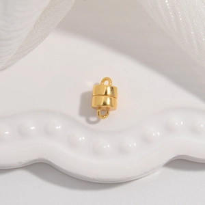 Detailed view of a golden cylindrical magnetic clasp with rings on a white ceramic plate