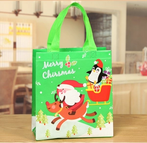 Detail of green non-woven Christmas gift bag with Santa and reindeer on wooden table