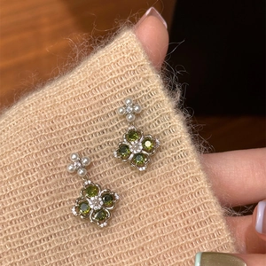 Macro shot of silver clover earrings with green gemstones and small pearls on a sweater