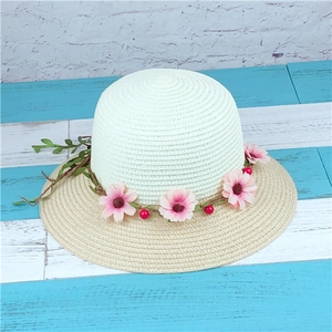 Detail of two-tone straw sun hat featuring pink fabric flowers and green leaves