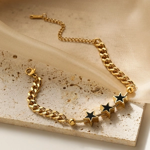 Gold star charm bracelet with black star pendants on elegant stone and silk fabric backdrop