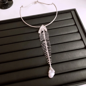 Detail of silver fishbone pendant necklace with white baroque pearl on a black jewelry tray