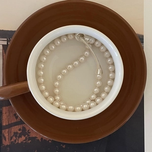 Close-up of elegant pearl necklace with silver buckle inside a white ceramic cup