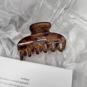 Close-up of tortoiseshell claw clip with gold Barrette La France text on white art paper