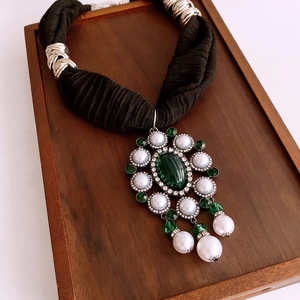 Macro view of French vintage necklace with green gemstone and pearl charms on wood