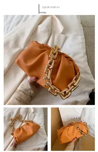 Detail of orange cloud bag featuring soft pleated leather and a thick gold chain strap