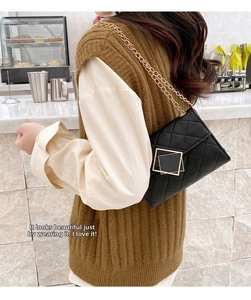 Detail of black quilted chain bag with gold square buckle worn in casual setting