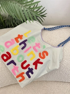 Light gray canvas tote bag with colorful letter embroidery and blue woven rope handles