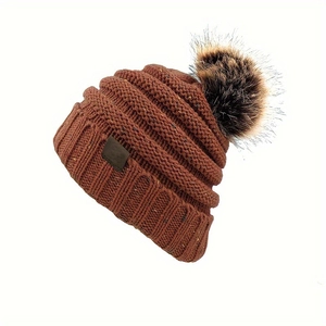 Détail du bonnet en maille caramel montrant les torsades et le pompon en fourrure