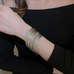 Detail of 20-piece layered gold metal bangle set on a black knit sleeve background