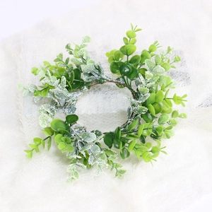 Close-up of frosted artificial eucalyptus leaves candle ring on white plush background