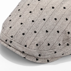 Macro view of grey herringbone fabric with black heart embroidery on the beret hat