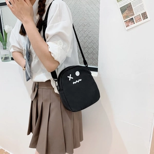 Détail d'un sac bandoulière en toile noire avec broderie de dessin animé minimaliste