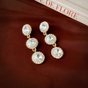 Détail de boucles d'oreilles pendantes dorées avec cristaux sur fond de soie rouge élégant