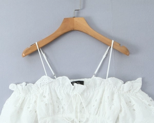 Detalle del top blanco de bordado suizo con cuello de volantes y cordones frontales