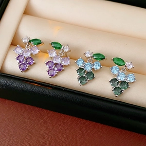 Close-up of sparkling zircon grape earrings in purple and blue on beige jewelry cushion