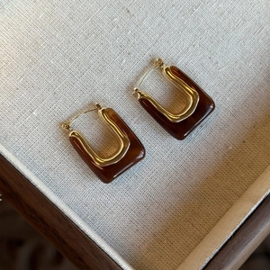 Detail view of square U-shaped earrings in gold metal and dark brown vintage resin