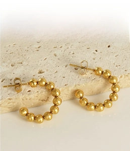 Detail of 18K gold beaded C-shape earrings on a beige travertine stone display