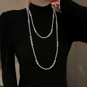 Detail of multi-layered long pearl necklace with white round beads on a black sweater