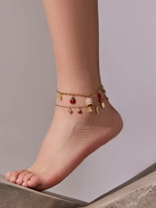 Détail d'une chevillère dorée avec pendentifs piment rouge, coccinelle et boule de cristal