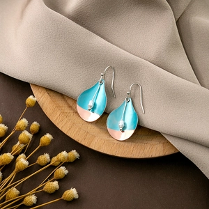 Detail of teardrop earring with turquoise and rose gold finish on a wooden base