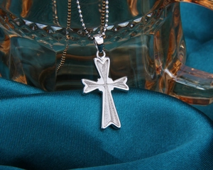 Détail macro du pendentif croix en argent avec texture givrée sur fond de soie bleue