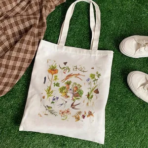 White canvas tote bag with hand-drawn strawberry and rabbit prints on grass background