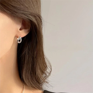 Detail of silver twisted knot hoop earring worn by a model in soft natural light