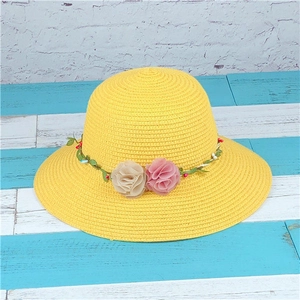 Detailed view of yellow woven straw hat featuring soft pink and beige fabric floral trim