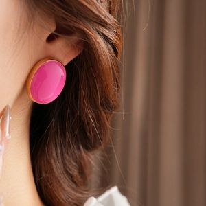 Close-up of pink enamel round stud earrings with gold trim worn by a model