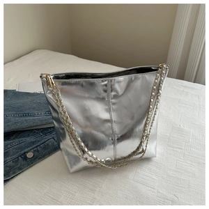 Detail of silver metallic bucket bag with gold chain strap on soft white bedding