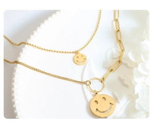 Detalle de collar de dos capas en acero de titanio dorado con colgante smiley Good Luck